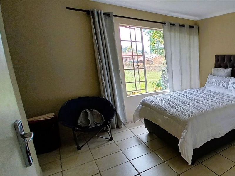 A bedroom featuring tiled flooring and a window with security bars, providing natural light and a view of the exterior.
