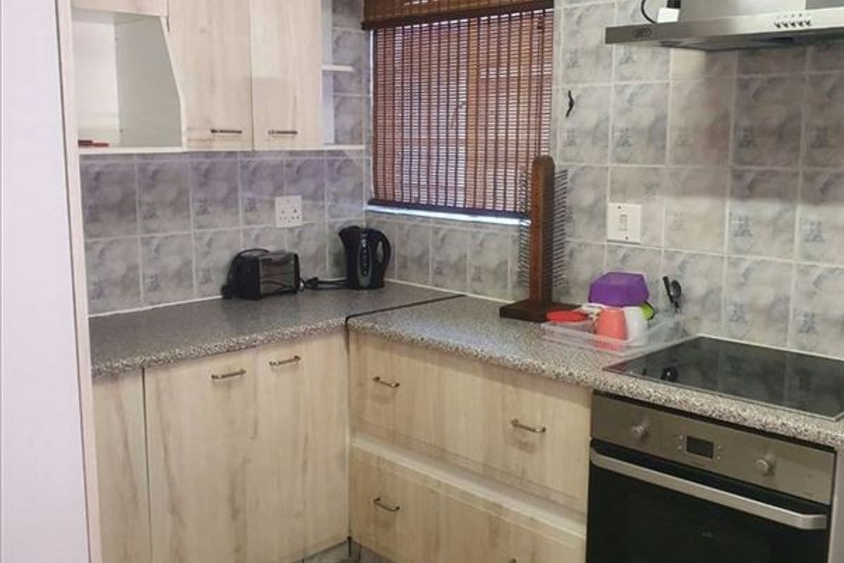 Compact kitchen featuring light wood-look cabinetry, laminate countertops, built-in oven, electric hob, and stainless steel extractor fan with tiled splashback.