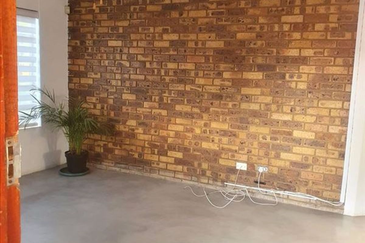 A bright living area featuring a rustic exposed brick feature wall, polished concrete flooring, and a ceiling fan.