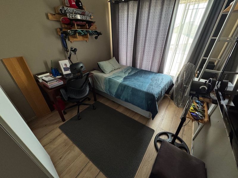 A compact bedroom featuring laminate flooring and large windows with curtains, providing natural light and access to the exterior.
