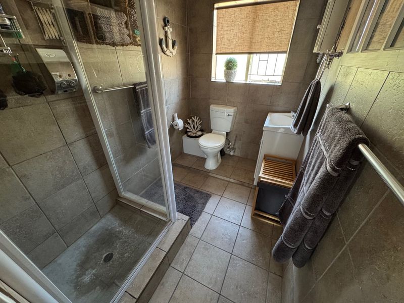A functional bathroom featuring a glass-enclosed shower, tiled walls and floors, a standard toilet, and a vanity basin.