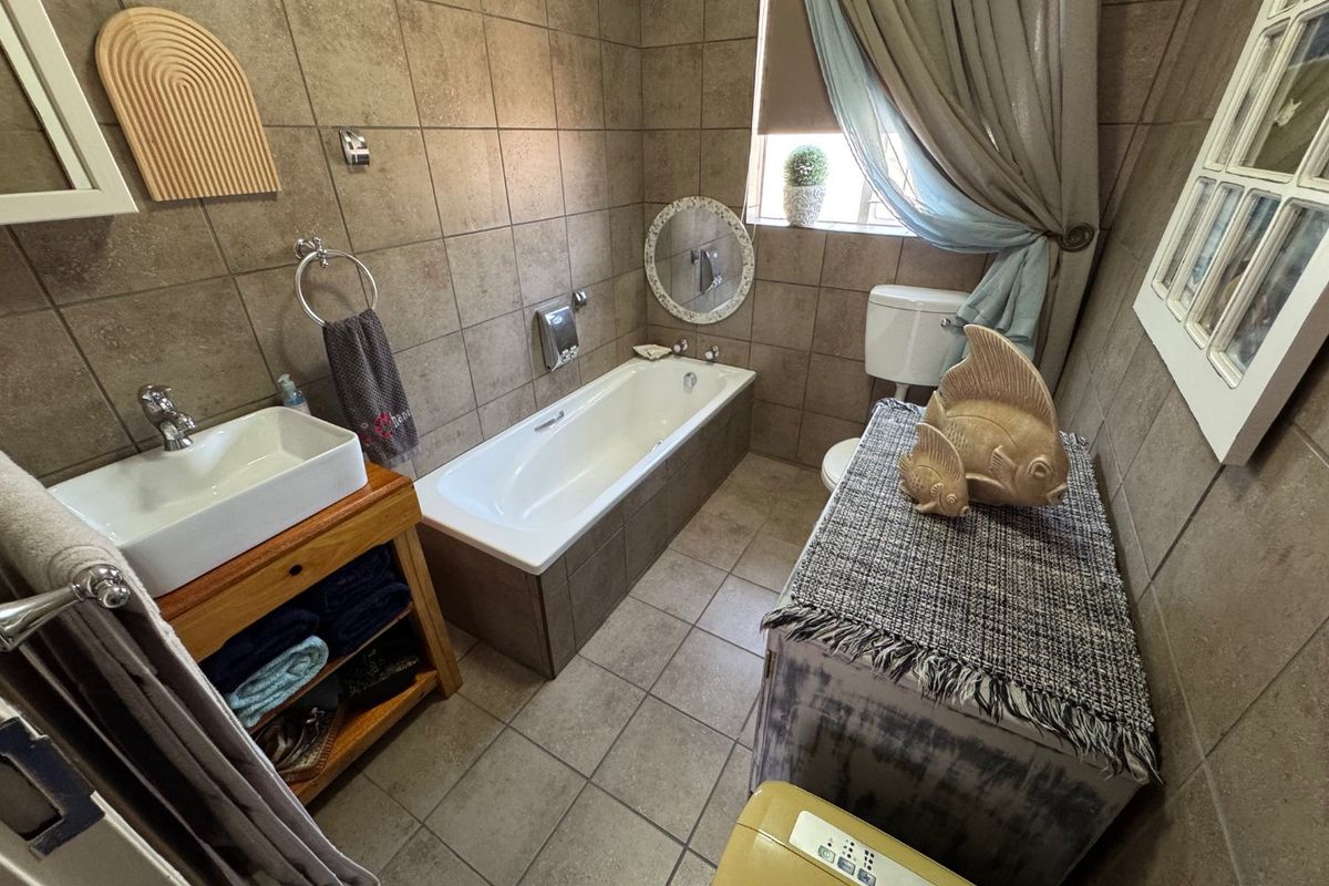 A functional bathroom featuring full-height ceramic wall tiling, a built-in bathtub, a vessel sink on a wooden vanity, and a standard toilet.