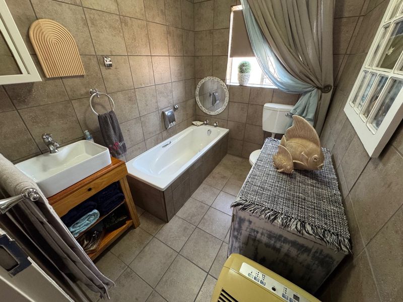 A functional bathroom featuring full-height ceramic wall tiling, a built-in bathtub, a vessel sink on a wooden vanity, and a standard toilet.