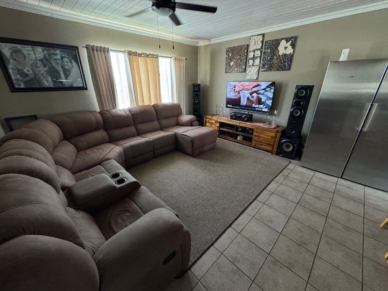 A spacious living room featuring tiled flooring, a tongue and groove ceiling, and a ceiling fan, providing a comfortable and functional family area.