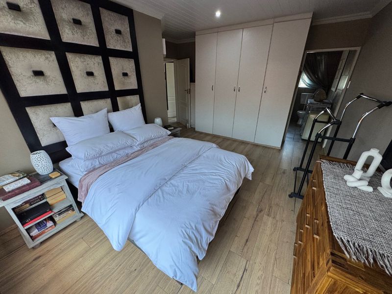 Spacious bedroom featuring light wood-look laminate flooring, ample built-in cupboard storage, and a tongue and groove ceiling, with an en-suite bathroom visible.