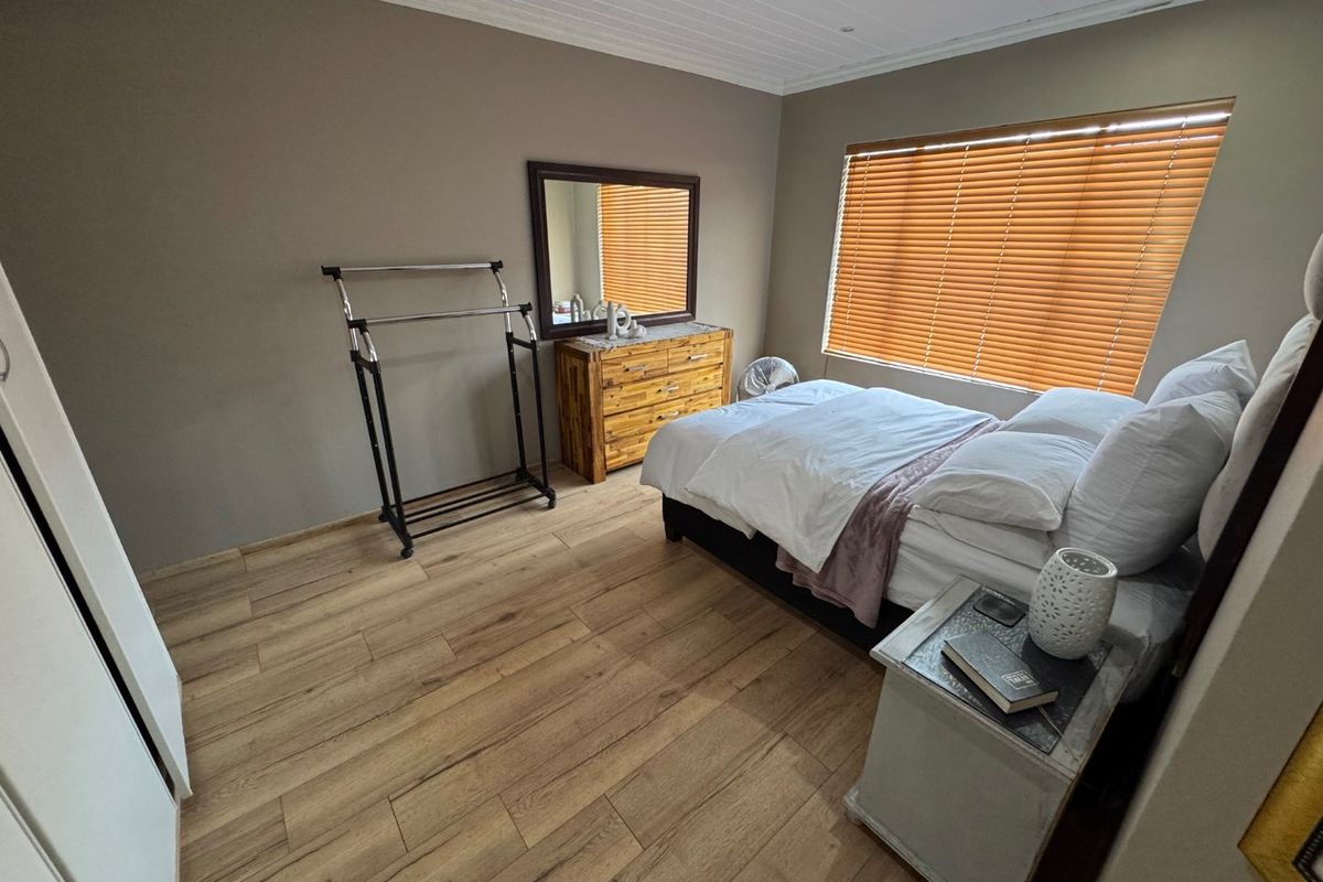 A bedroom featuring light-toned laminate flooring, a tongue and groove ceiling, and timber venetian blinds providing natural light control.