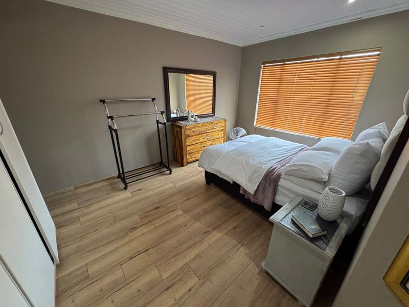 A bedroom featuring light-toned laminate flooring, a tongue and groove ceiling, and timber venetian blinds providing natural light control.