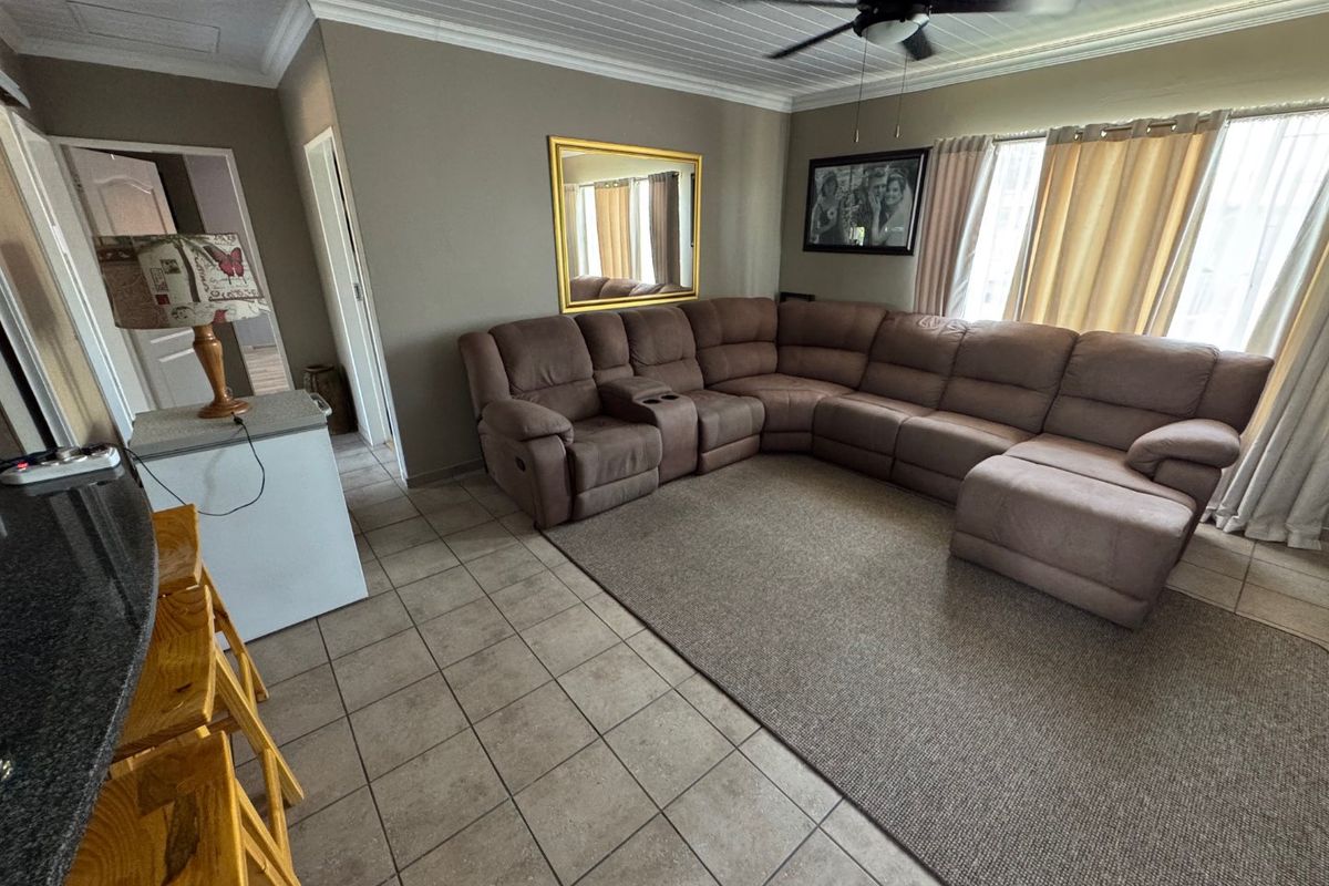 A spacious living area featuring tiled flooring, a tongue and groove ceiling with a fan, and a breakfast bar with a granite countertop.