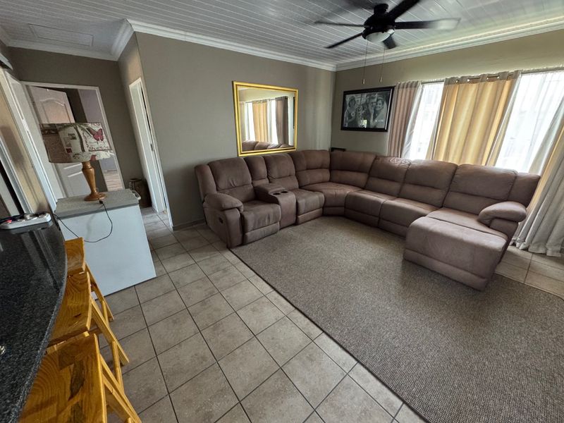 A spacious living area featuring tiled flooring, a tongue and groove ceiling with a fan, and a breakfast bar with a granite countertop.
