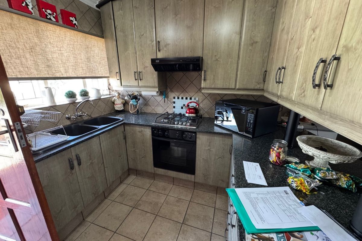 A functional kitchen featuring laminate cabinetry, granite countertops, a gas hob with extractor fan, and a double basin sink with tiled backsplash.