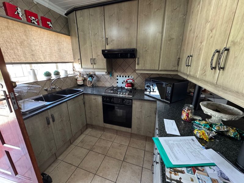 A functional kitchen featuring laminate cabinetry, granite countertops, a gas hob with extractor fan, and a double basin sink with tiled backsplash.