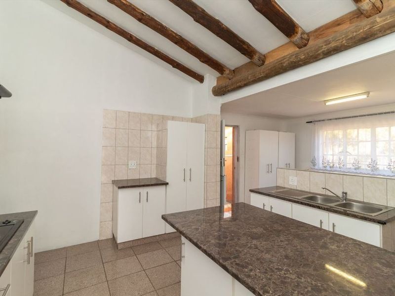 Open-plan kitchen featuring exposed timber ceiling beams, granite countertops, built-in cabinetry, and a double stainless steel sink with tiled splashbacks.