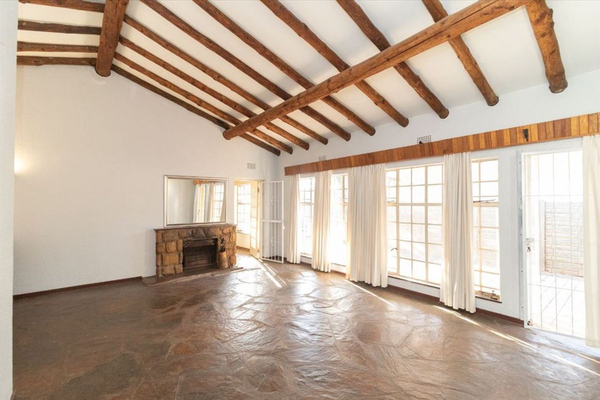 Spacious living room featuring exposed timber ceiling beams, a rustic stone fireplace, and durable flagstone flooring with abundant natural light from large windows.