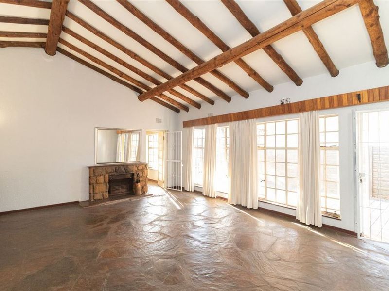 Spacious living room featuring exposed timber ceiling beams, a rustic stone fireplace, and durable flagstone flooring with abundant natural light from large windows.
