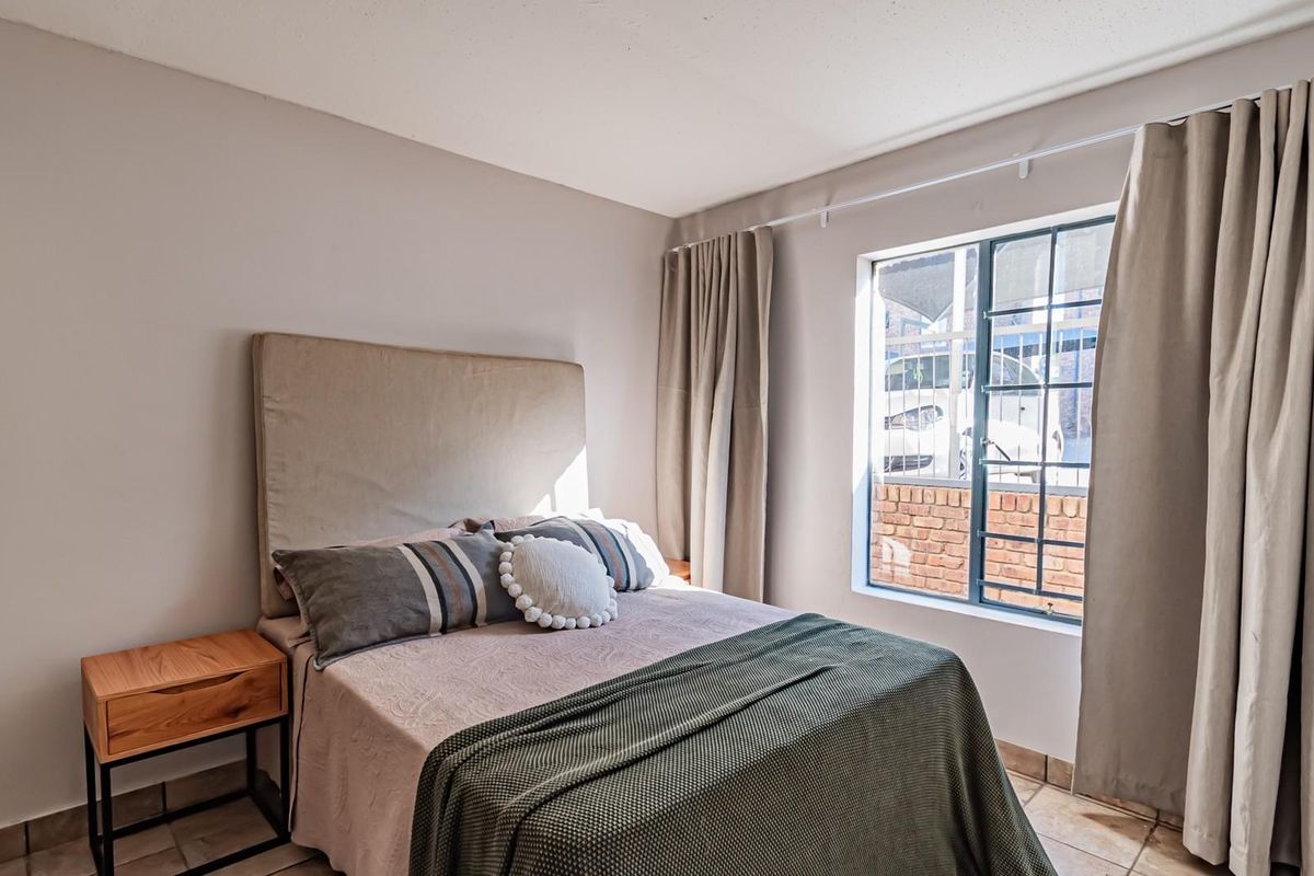 A well-lit bedroom featuring tiled flooring and a window fitted with security bars, offering a clean and functional living space.