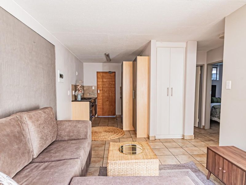 Open-plan living area featuring tiled flooring, built-in storage cupboards, and a compact kitchen space with integrated oven and hob.