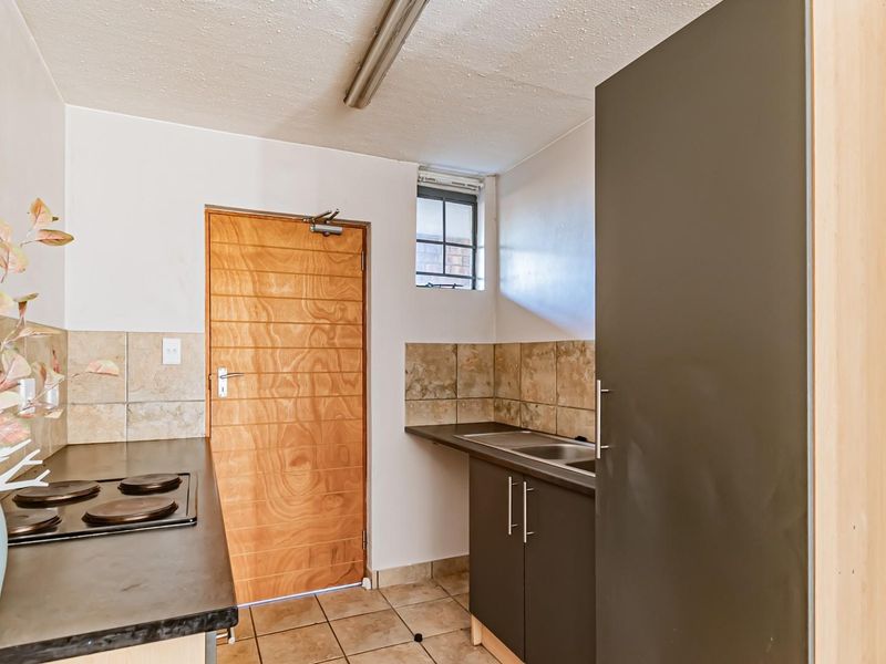 A functional kitchen featuring built-in cabinetry, laminate countertops, a stainless steel sink, and an electric hob with tiled splashbacks.