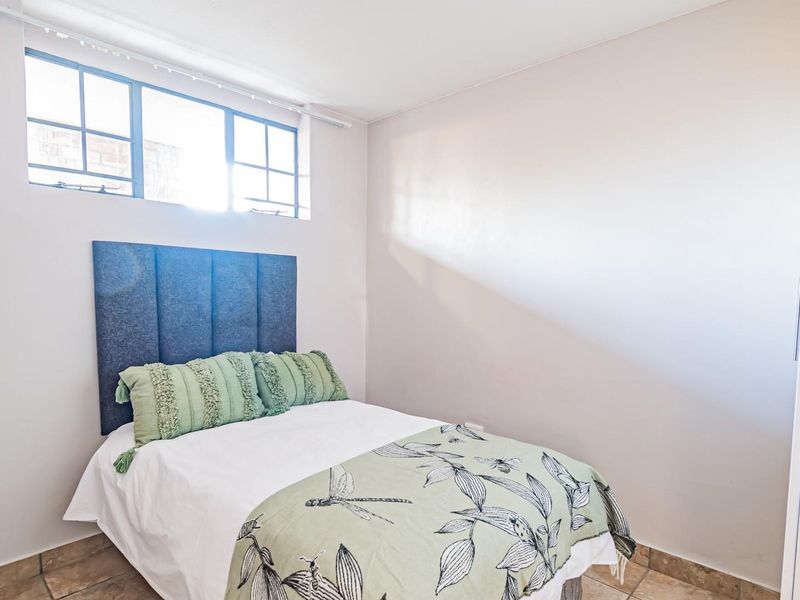 A compact bedroom featuring tiled flooring, a high-level window for natural light, and a built-in wardrobe.