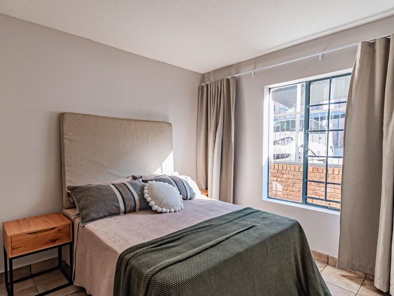 A well-lit bedroom featuring tiled flooring and a window fitted with security bars, providing a comfortable and functional living space.