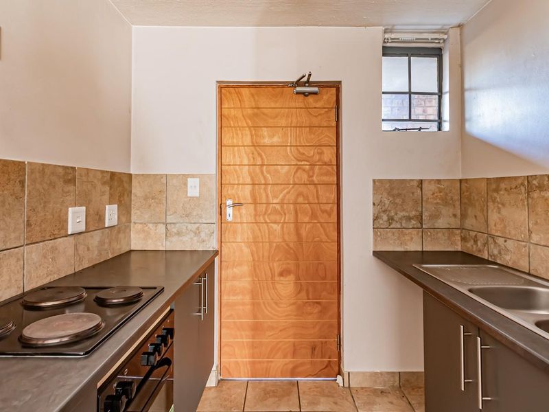 A functional kitchen featuring built-in cabinetry, a stainless steel sink, electric hob, oven, and tiled finishes, offering a clean and practical workspace.