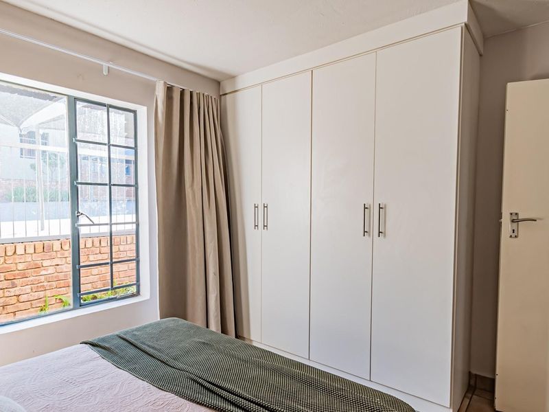 A well-maintained bedroom featuring built-in cupboards and a grid-pane window providing natural light.
