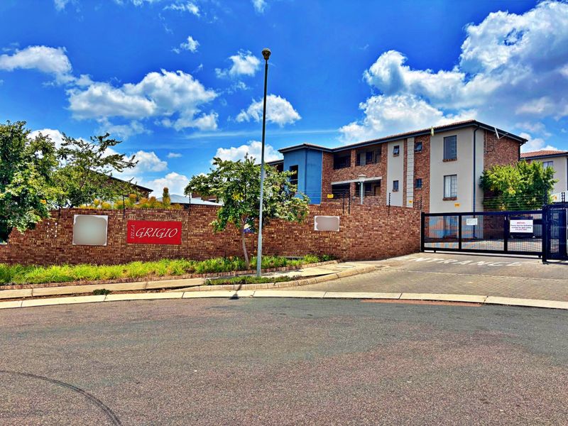 Front entrance view of Villa Grigio apartment complex, featuring a brick boundary wall, secure gated access, and paved driveway.