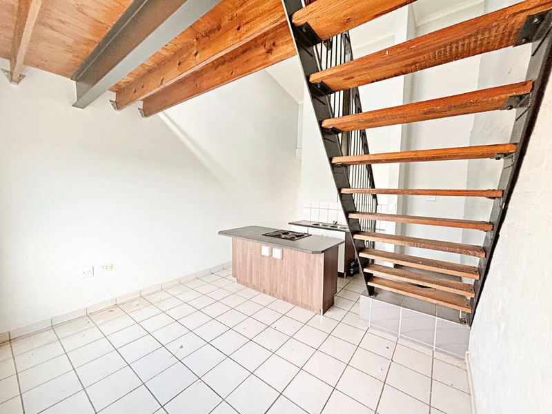 Open plan living area featuring a central kitchen island with built-in hob, tiled flooring, and an industrial-style staircase with timber treads.