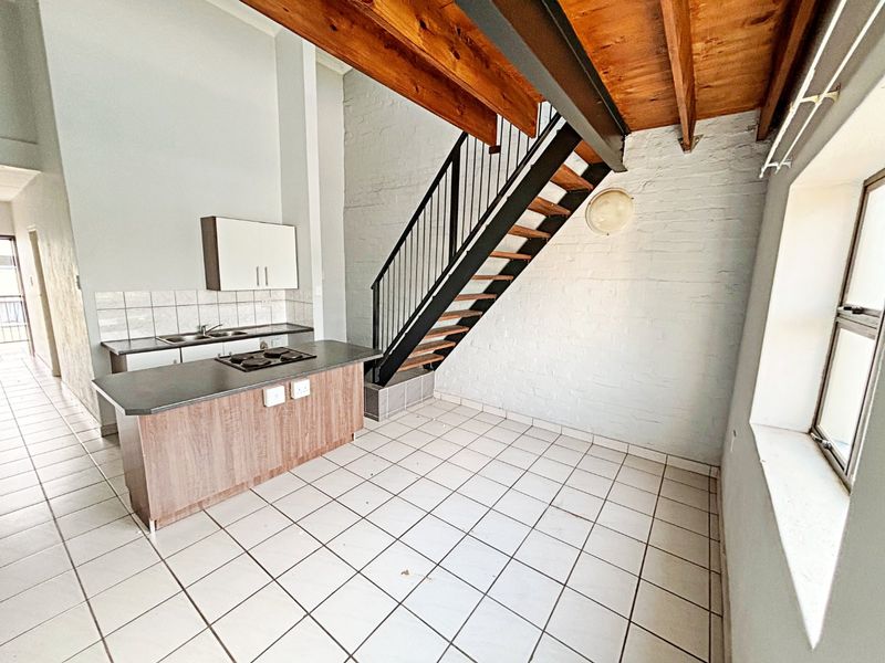 Open-plan kitchen and living area featuring a central island with built-in hob, exposed timber ceiling beams, and a staircase leading to the upper level.