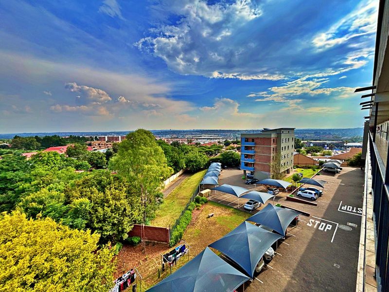 Elevated view overlooking the apartment complex parking area with shade cloth carports and surrounding neighborhood landscape.