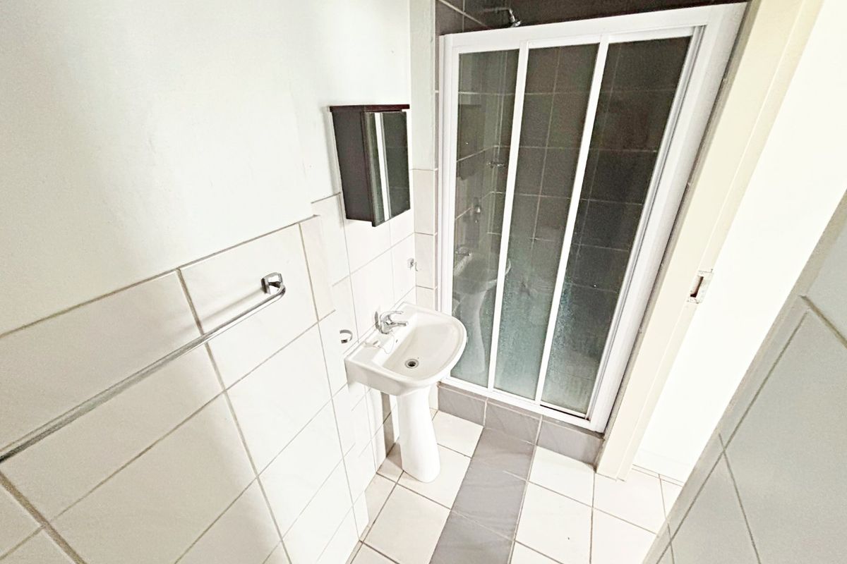 A functional bathroom featuring a pedestal basin, a shower enclosure with sliding doors, and neutral wall and floor tiling.