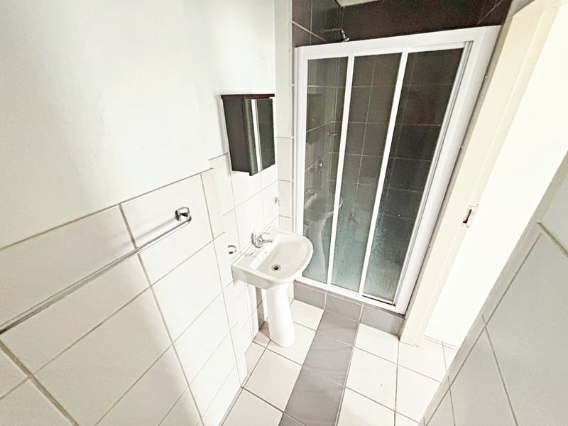 A functional bathroom featuring a pedestal basin, a shower enclosure with sliding doors, and neutral wall and floor tiling.