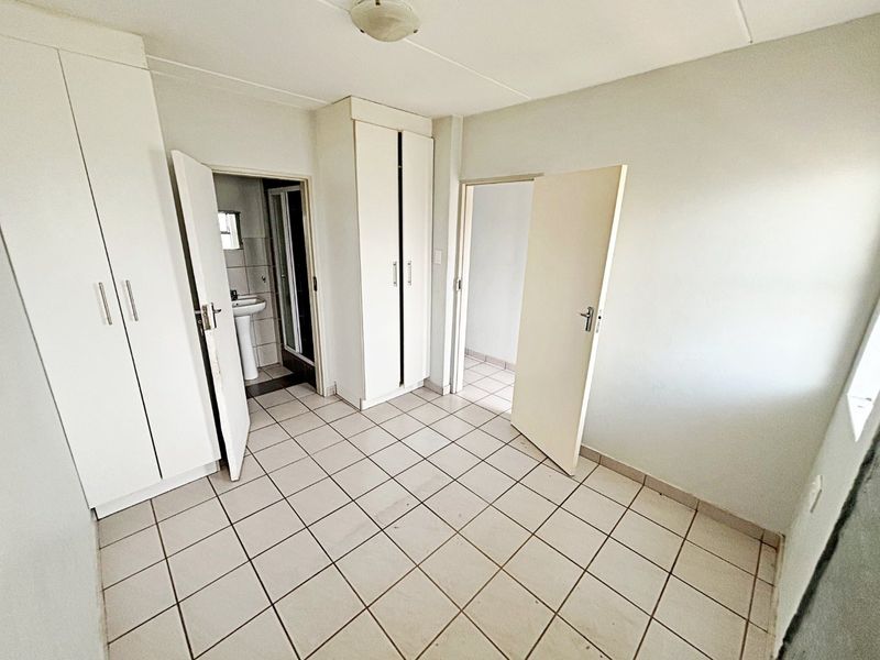 An empty bedroom featuring tiled flooring and built-in cupboards, with direct access to an en-suite bathroom.