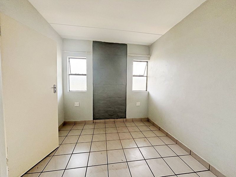 An empty bedroom featuring tiled flooring, two windows, and a central dark-painted feature wall section.