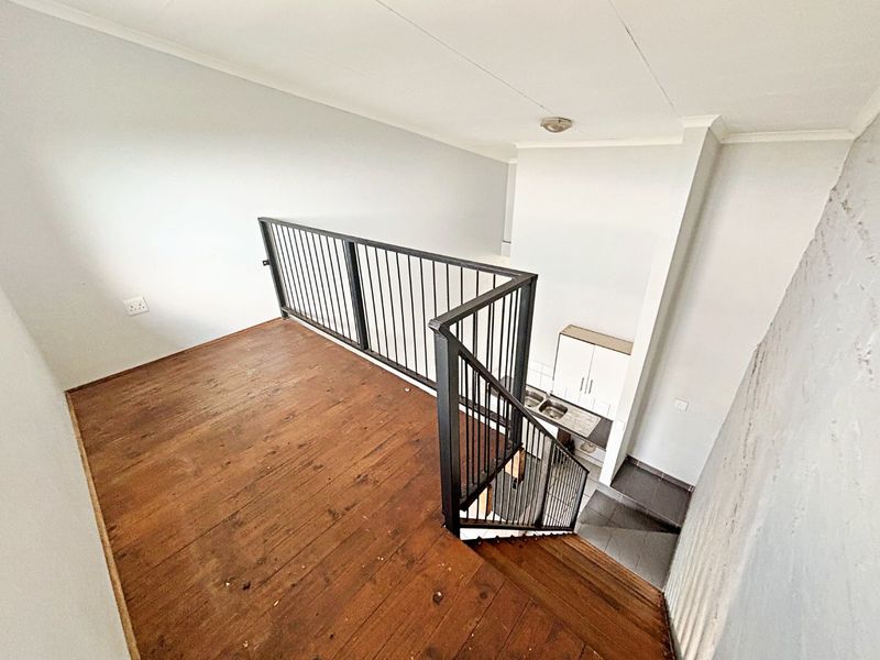 An open-plan loft area featuring timber flooring, a metal staircase balustrade, and a compact kitchenette with built-in cabinetry and a sink.