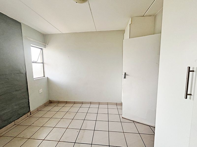 An empty bedroom featuring tiled flooring, a built-in cupboard, and a single window, offering a blank canvas for renovation or interior design.