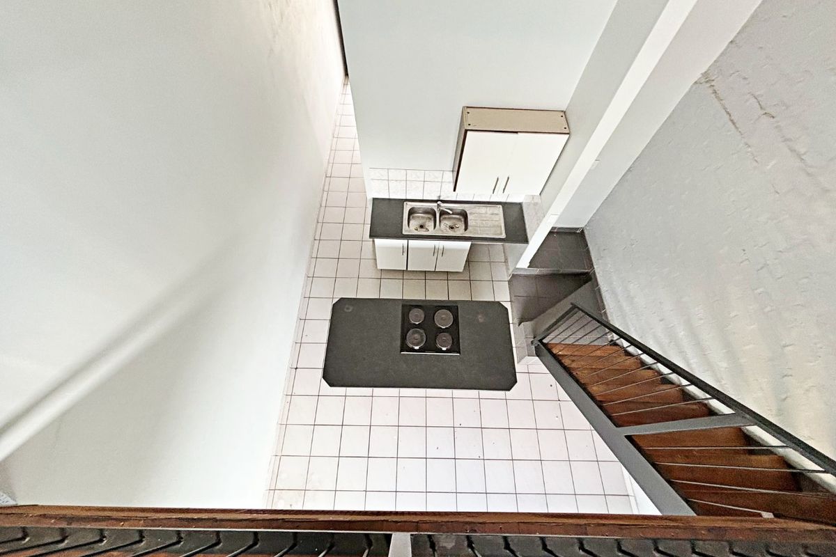 An elevated view of a compact kitchen featuring tiled flooring, built-in cabinetry, a double sink, and an electric hob, adjacent to a staircase.