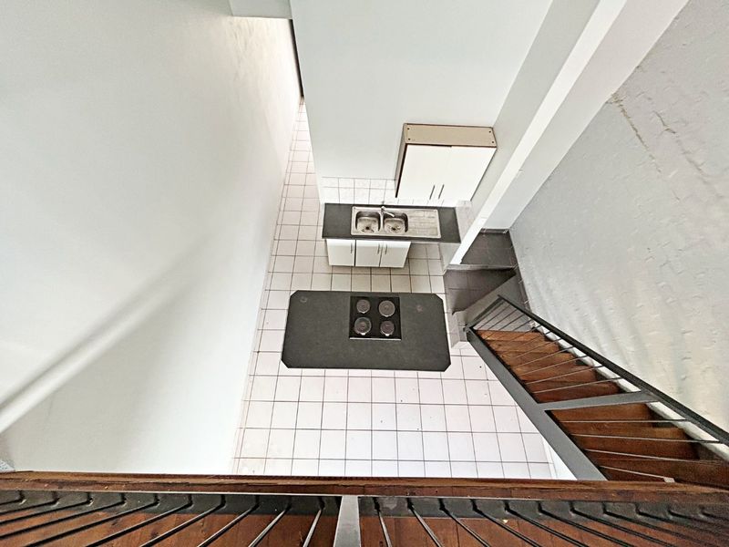 An elevated view of a compact kitchen featuring tiled flooring, built-in cabinetry, a double sink, and an electric hob, adjacent to a staircase.