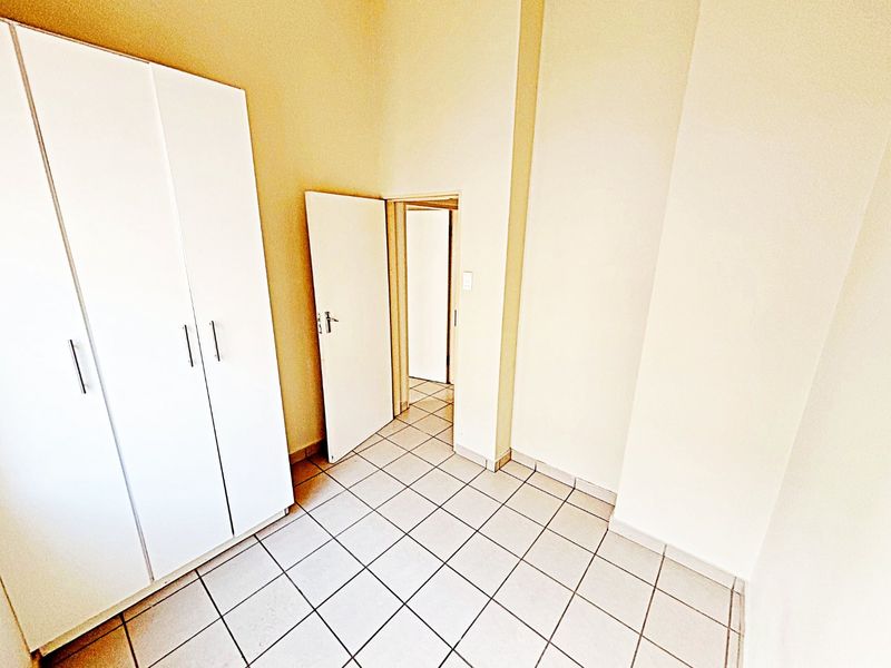 A bright, empty bedroom featuring neutral tiled flooring and a built-in white wardrobe, offering a clean and versatile space.