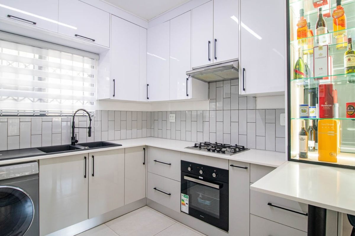 Modern kitchen featuring white gloss cabinetry, subway tile backsplash, quartz countertops, integrated appliances, and a built-in illuminated display cabinet.