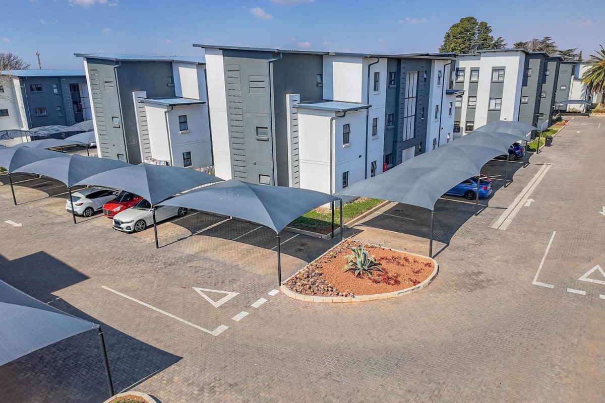 Aerial view of a modern apartment complex featuring paved parking bays with shade cloth carports and well-maintained exterior building facades.