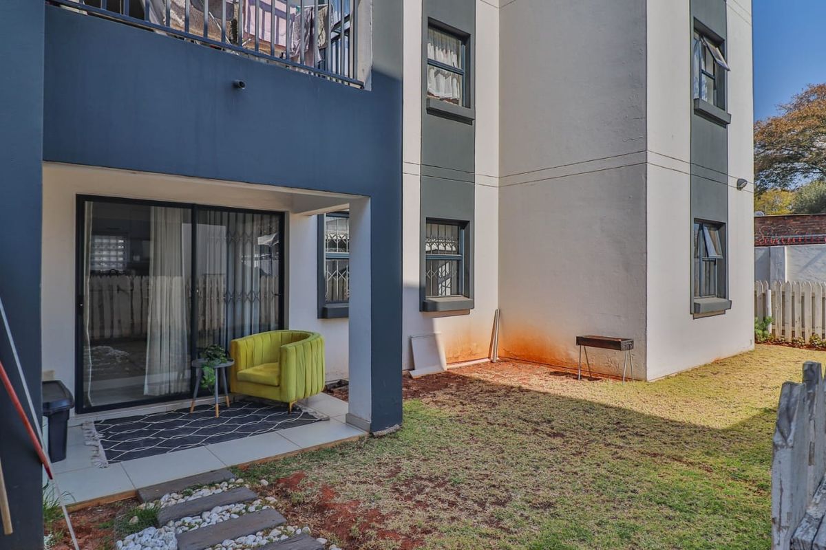 Rear view of an apartment building featuring a ground-floor patio with sliding doors, security bars, and a small private garden area.