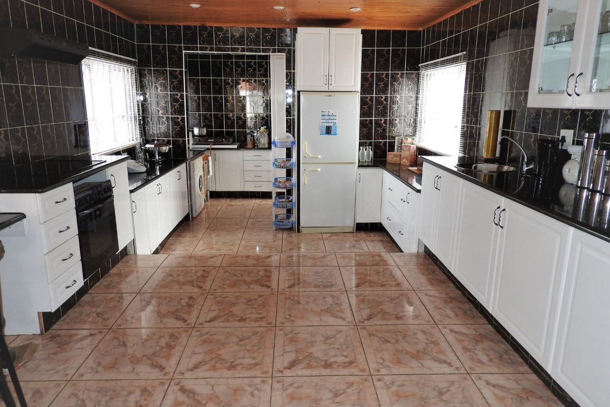 Spacious kitchen featuring white cabinetry, dark granite countertops, tiled finishes, and a timber ceiling, offering a functional layout with integrated appliances.