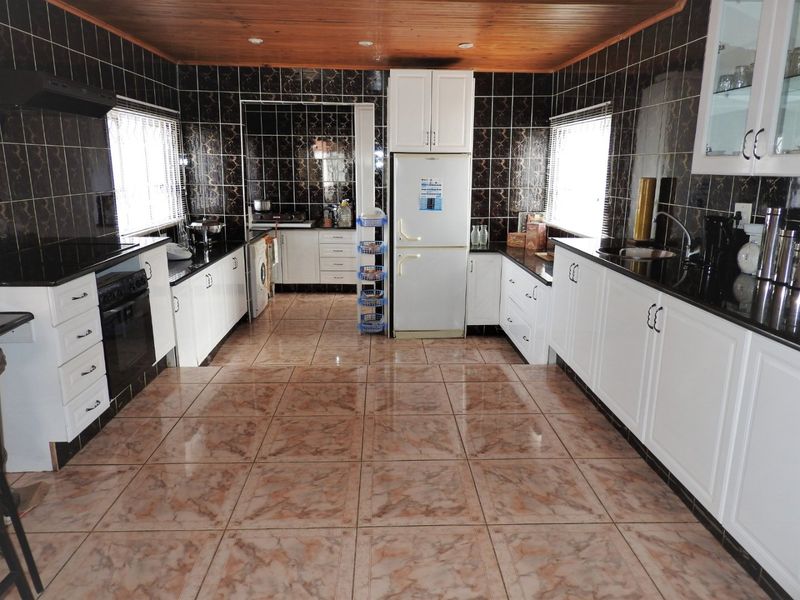 Spacious kitchen featuring white cabinetry, dark granite countertops, tiled finishes, and a timber ceiling, offering a functional layout with integrated appliances.