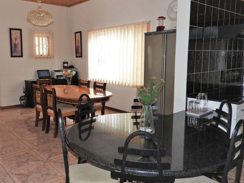 Open plan living and dining area featuring tiled flooring, a wooden ceiling, and a kitchen with black tiled backsplash and granite countertops.