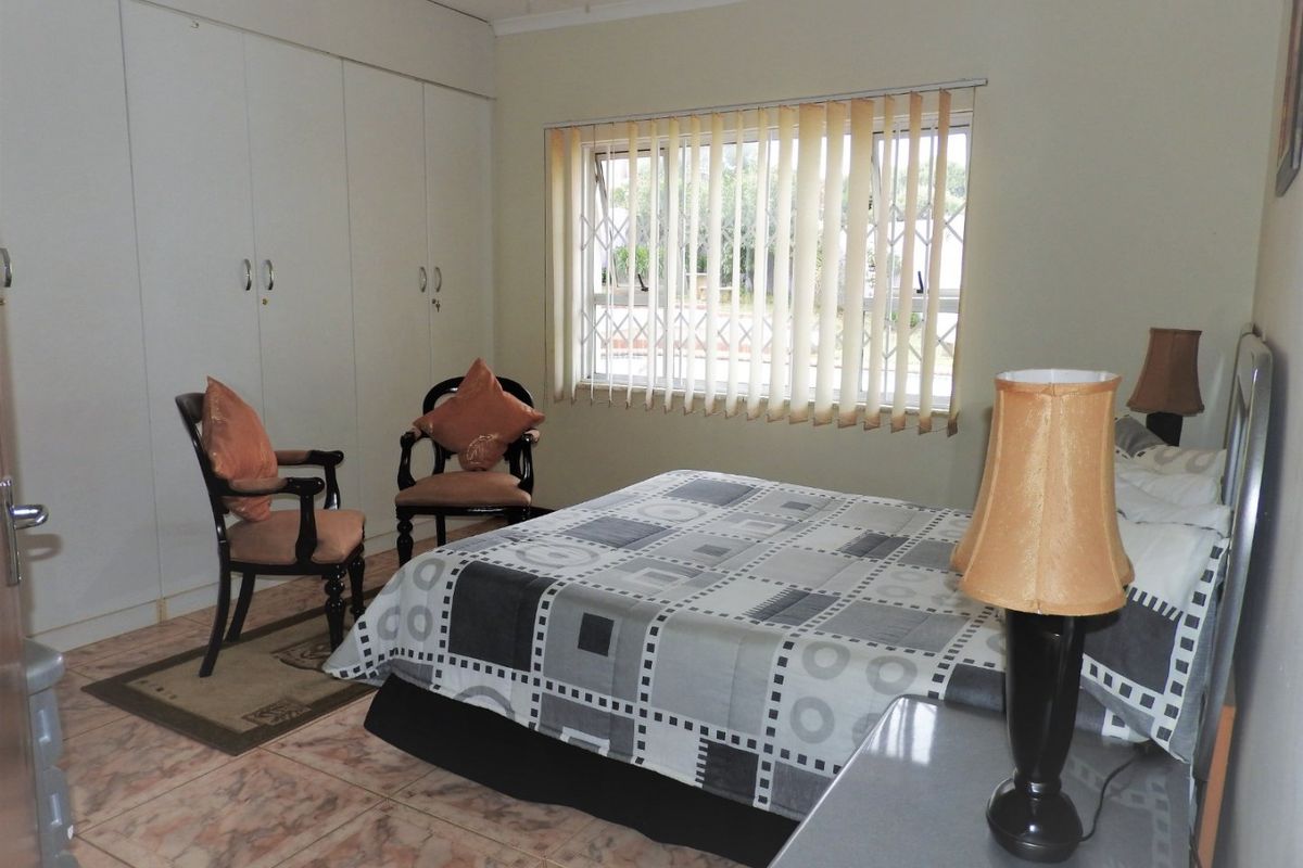 A functional bedroom featuring built-in cupboards, tiled flooring, and a ceiling fan, with natural light provided by a window fitted with vertical blinds.
