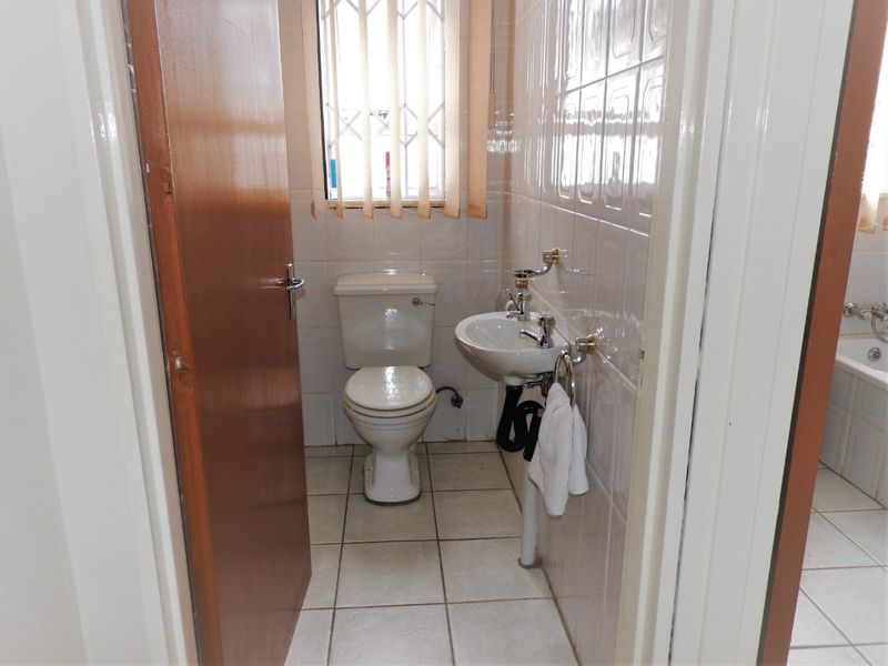A functional bathroom featuring tiled walls and flooring, equipped with a standard toilet and pedestal basin, with a window providing natural light.