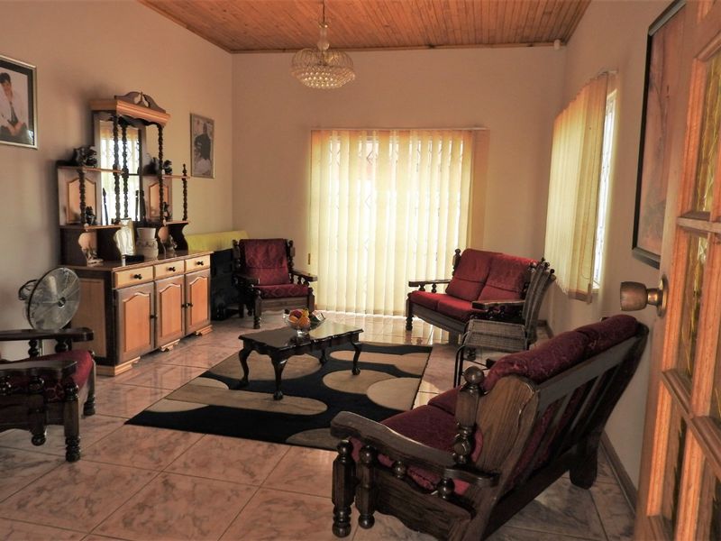 A living room featuring tiled flooring, a timber tongue and groove ceiling, and vertical blinds covering the sliding door.