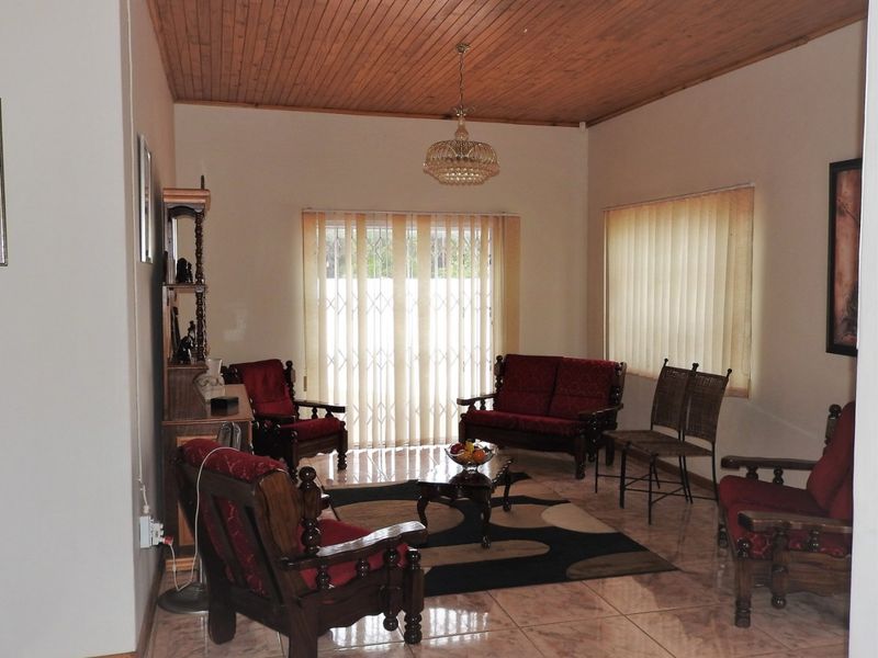 A living room featuring a timber tongue and groove ceiling, ceramic tiled flooring, and vertical blinds with an integrated security gate.