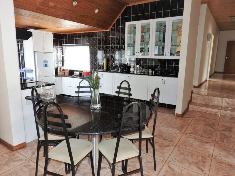 Open-plan kitchen and dining area featuring white cabinetry, granite countertops, dark tiled splashbacks, and a distinctive timber-clad ceiling.
