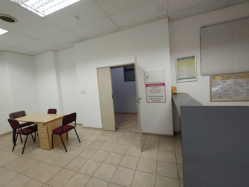A functional commercial office space featuring ceramic floor tiles, a built-in reception counter, and a suspended ceiling with recessed lighting.